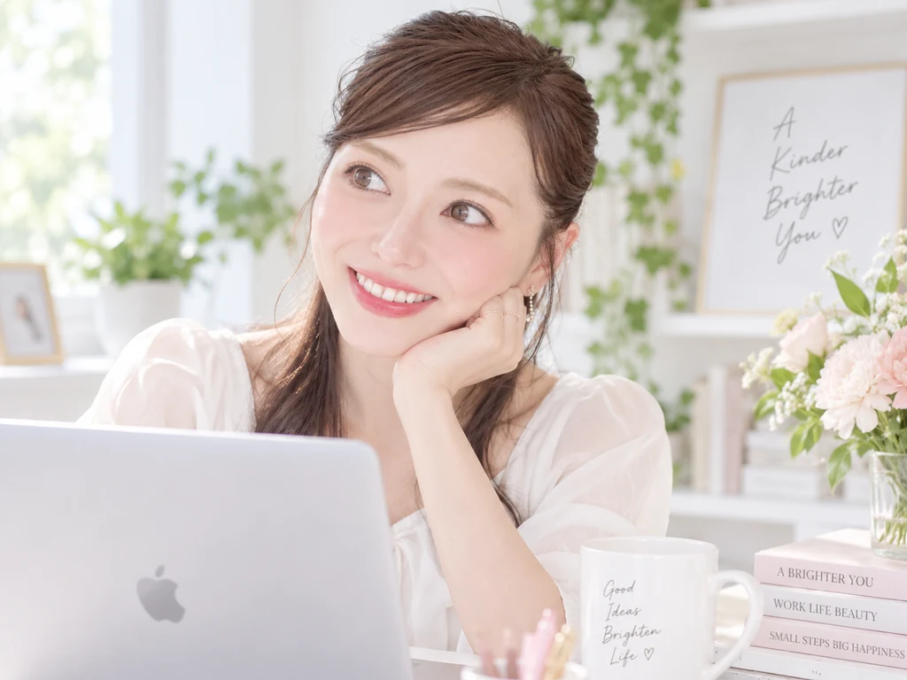 窓辺でMacBookに向かいながら、横を向いて微笑むMaiko